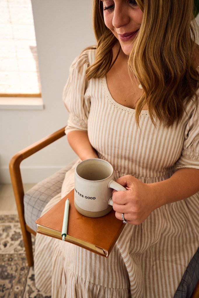 Kelsey smiling while journaling with a warm mug in hand